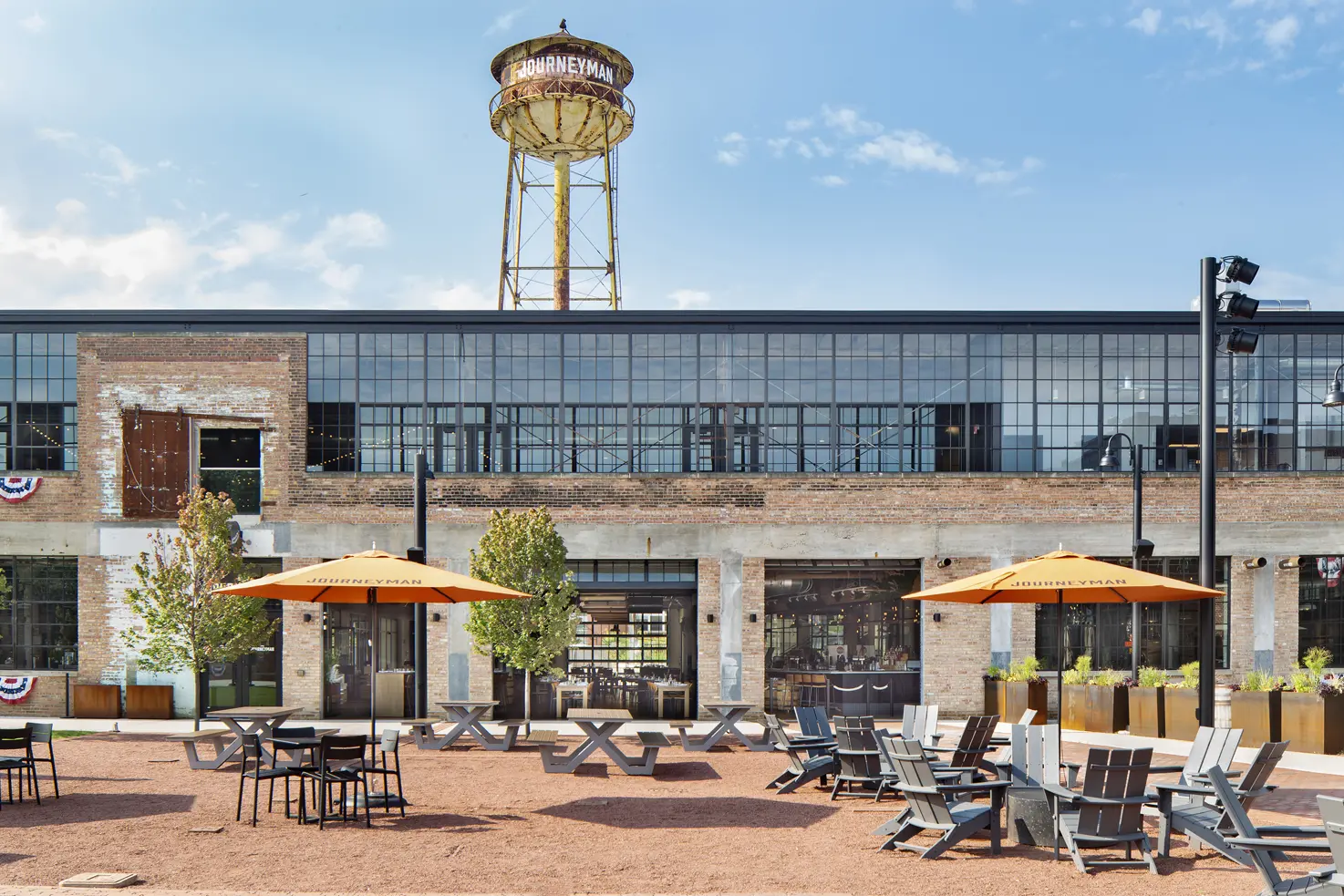 The American Factory building is shown with the water tower in the background. The courtyard is shown with tables and chairs throughout.